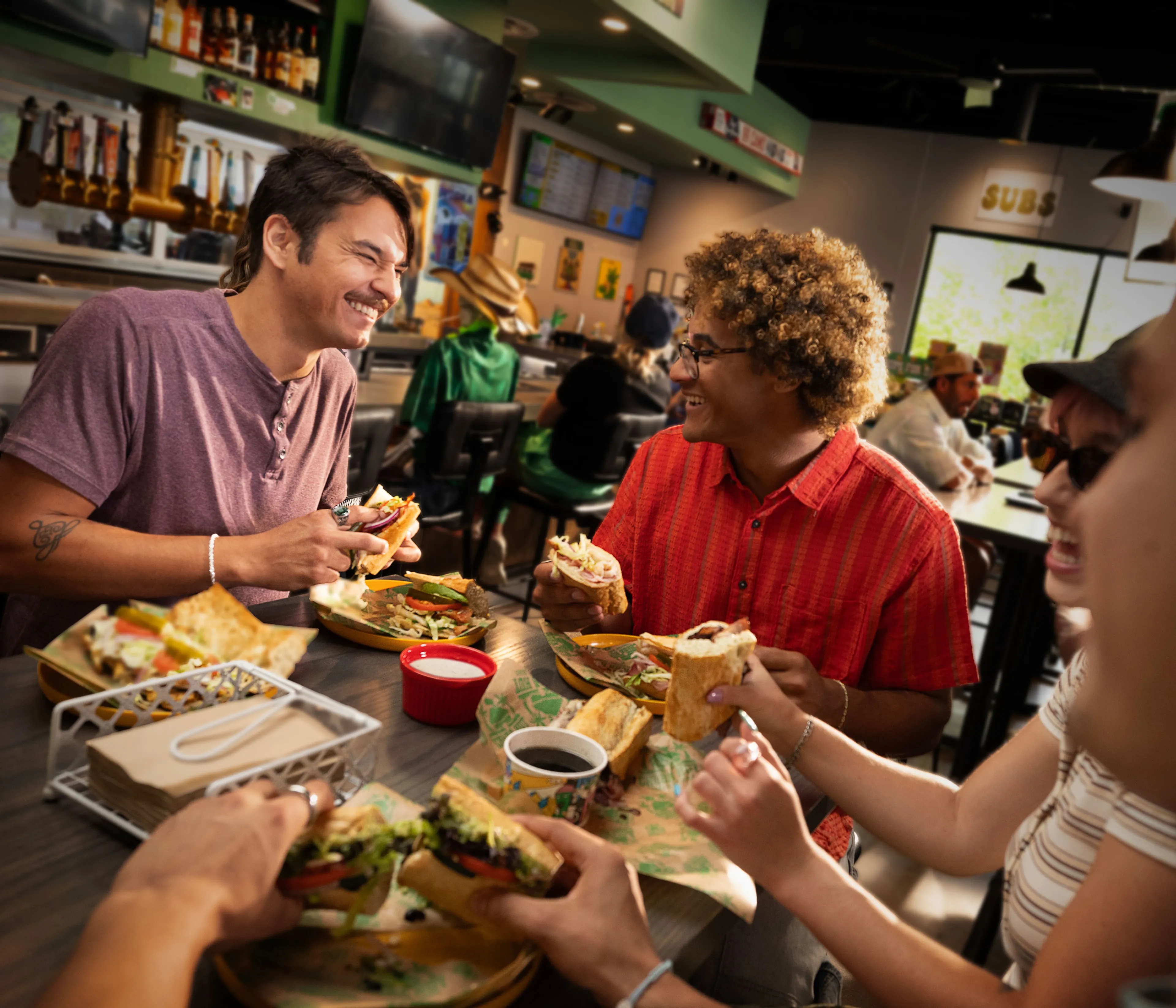Friends sharing toasted subs inside a Cheba Hut shop