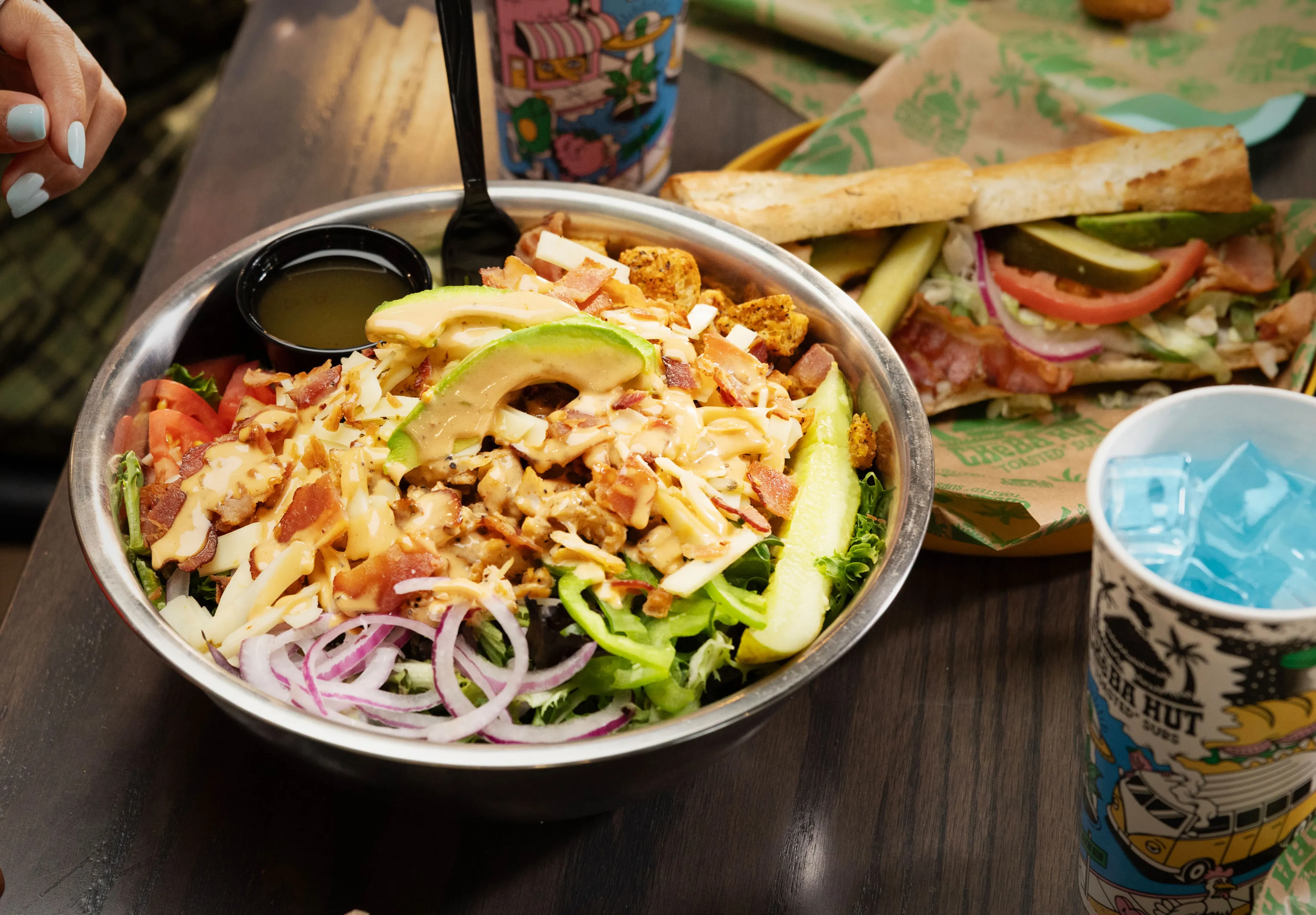Loaded salad with grilled chicken, bacon, cheese, avocado, and vegetables beside a Cheba Hut drink