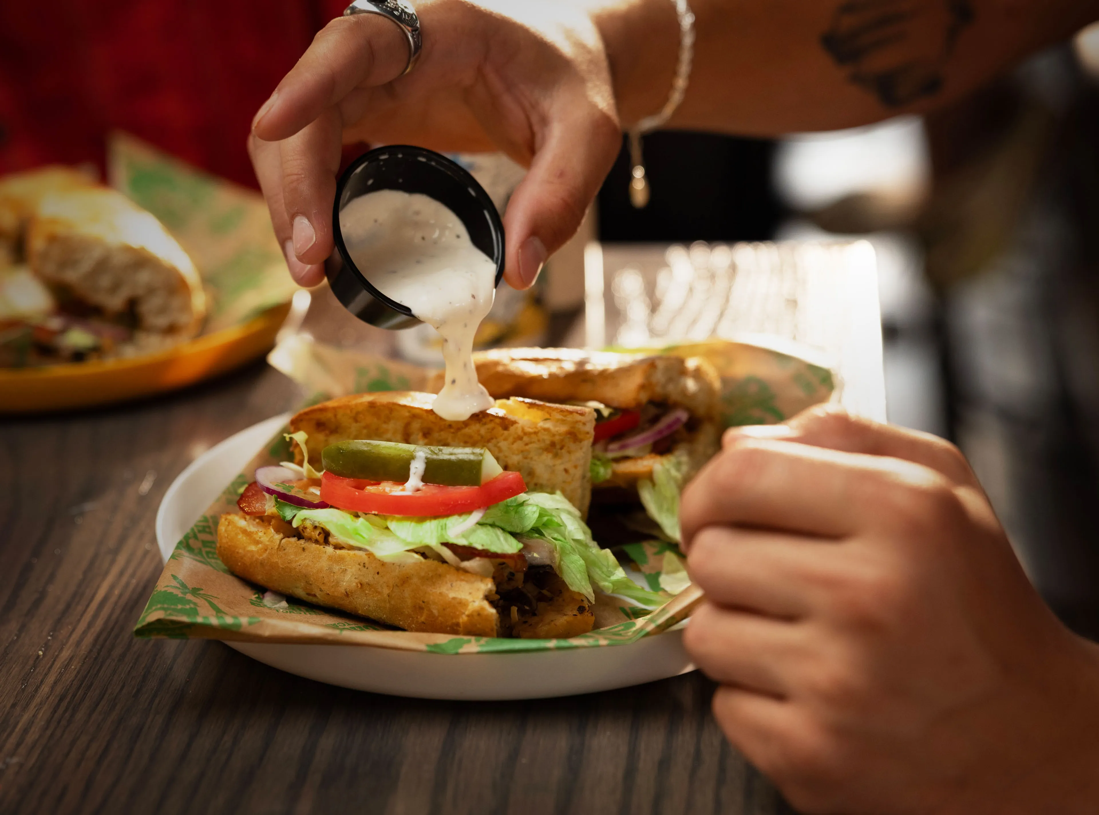 Person pouring creamy sauce over toasted Cheba Hut subs