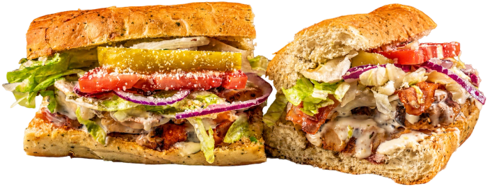 Two loaded toasted subs with fresh vegetables, pickles, and creamy sauce