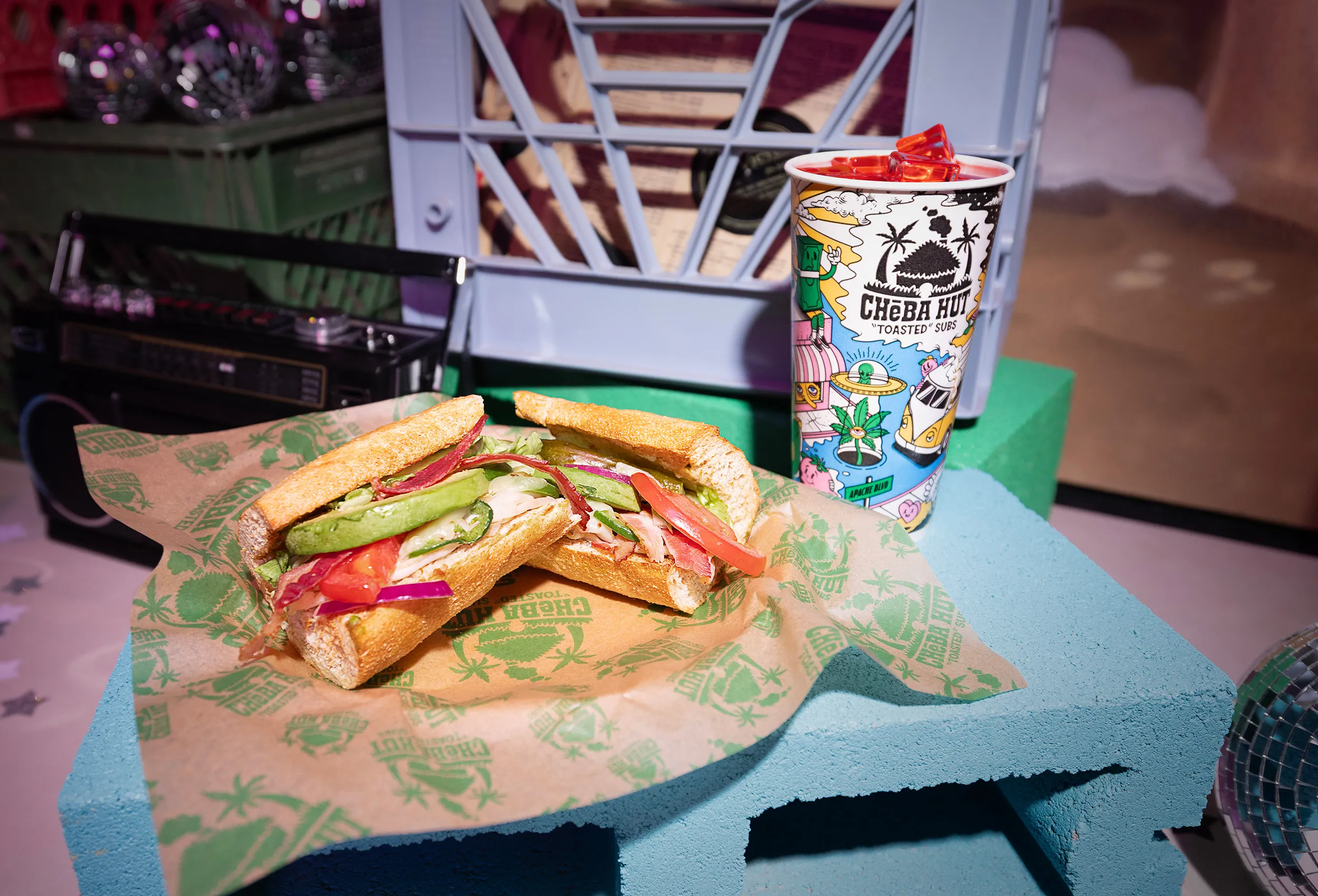 Two toasted Cheba Hut subs and a colorful drink on a blue table