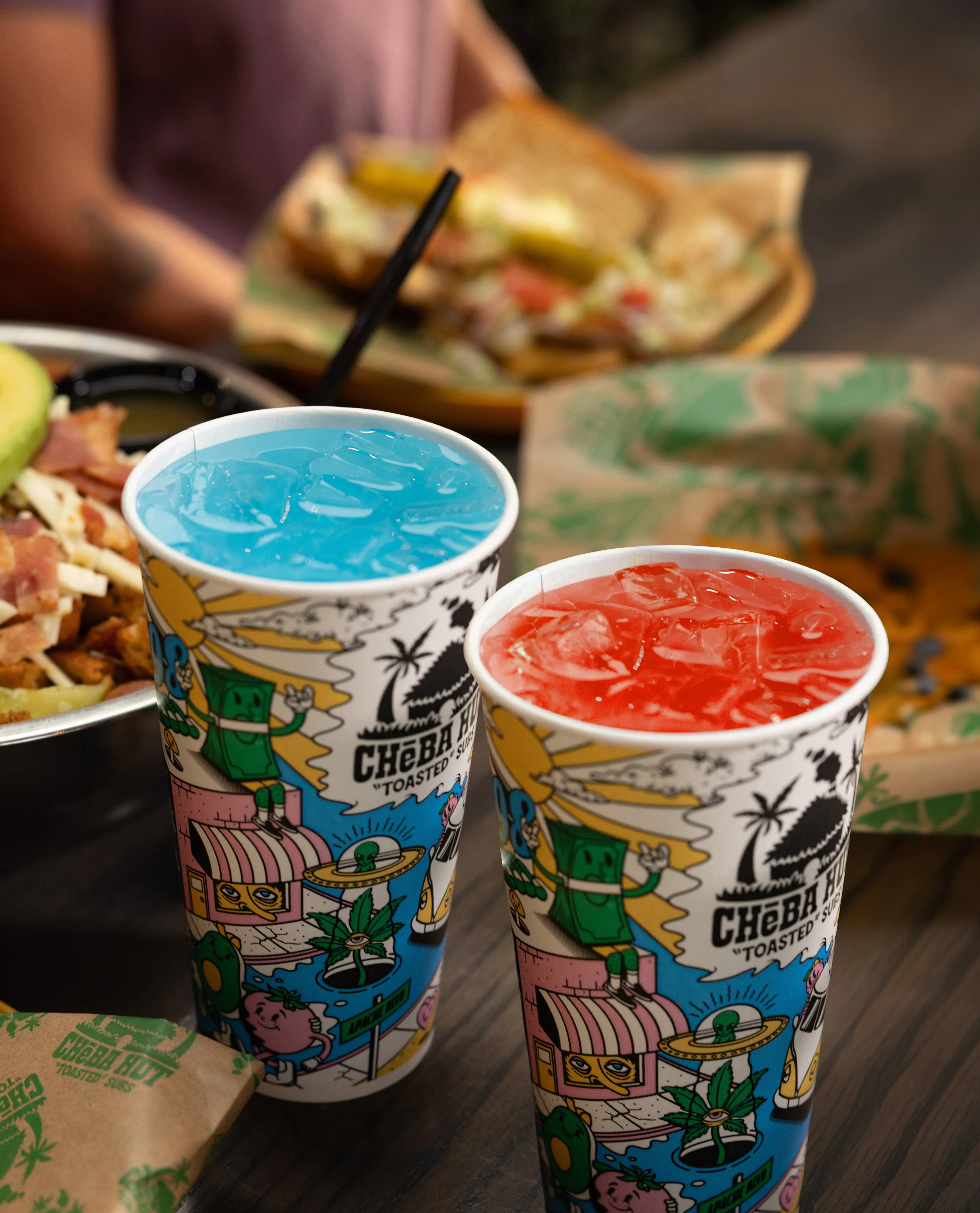 Two colorful Cheba Hut fountain drinks sitting in front of some Cheba Hut toasted subs